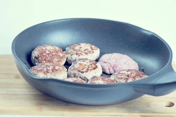 Tavada pirzola. Ahşap bir yüzeyüzerinde kızartma tavası. Pirzolalardan biri çiğ, gerisi kızartılır. Close.