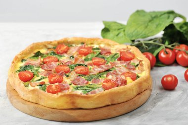 Klasik Fransız pasta kish. Krema, tavuk yumurtası, ıspanak ve pastırma ile dolum. Çerçevepeçende, yumurtalarda. bıçak ve kiraz domates. Close.