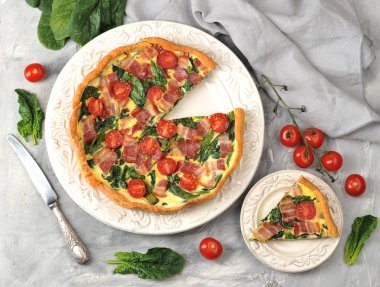 Krem, tavuk yumurtası, ıspanak ve pastırma doldurma ile kish açık pasta. Bir parça pastayla tabağın yanında. Çerçevede, bir bıçak, bir kiraz domates dalı ve ıspanak yaprakları. Yukarıdan görüntüle.