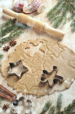 Noel kurabiyeleri pişiriyorum. Hamur ve kurabiye kesiciler. Ladin dalları, tarçın, anason kompozisyonu tamamlar. Dikey çerçeve yönlendirmesi. Açık arka plan.