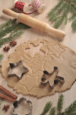 Noel kurabiyeleri pişiriyorum. Hamur ve kurabiye kesiciler. Ladin dalları, tarçın, anason kompozisyonu tamamlar. Dikey çerçeve yönlendirmesi. Açık arka plan.