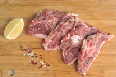 Tahta bir tahta üzerinde biftek şeklinde ham koyun eti. Koyun etinin yanında bir dilim limon ve biber li tuz var. Yukarıdan görüntüleyin. Close.