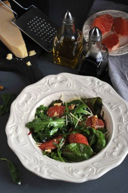 Pembe greyfurtlu salata. Bir parça Parmesan peyniriyle tahtanın yanında. Çerçevede ceviz, zeytinyağı ve balzamik sirke ile şişe. Dikey çekim. 