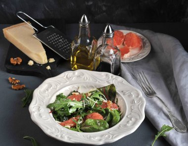 Pembe greyfurtlu salata. Bir parça Parmesan peyniri ve greyfurt dilimleri ile bir tabak ile tahta yakınında. Çerçevede ceviz, zeytinyağı, balsamik, çatal ve peçete ile şişe. Close.