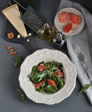 Pembe greyfurtlu salata. Bir parça Parmesan peyniriyle tahtanın yanında. Çerçevede ceviz, zeytinyağı ve balzamik sirke ile şişe. Yukarıdan görüntüleyin. Dikey çekim. 