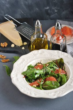 Pembe greyfurtlu salata. Bir parça Parmesan peyniriyle tahtanın yanında. Çerçevede ceviz, zeytinyağı ve balzamik sirke ile şişe. Dikey çekim.