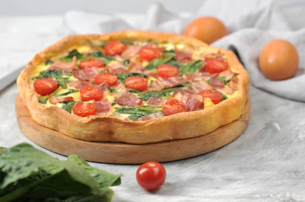 Klasik Fransız pasta kish. Krema, tavuk yumurtası, ıspanak ve pastırma ile dolum. Çerçevede, bir demet yeşil ıspanak ve çeri domates. Close.