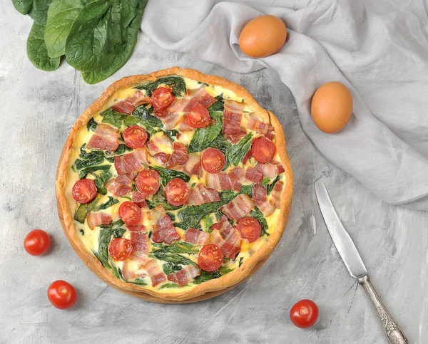 Klasik Fransız pasta kish. Krema, tavuk yumurtası, ıspanak ve pastırma ile dolum. Çerçevepeçende, yumurtalarda. bıçak ve kiraz domates. Yukarıdan görüntüleyin. Close.