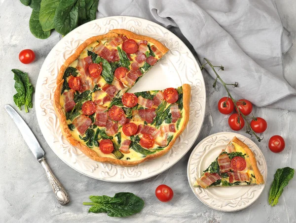 Krem, tavuk yumurtası, ıspanak ve pastırma doldurma ile kish açık pasta. Bir parça pastayla tabağın yanında. Çerçevede, bir bıçak, bir kiraz domates dalı ve ıspanak yaprakları. Yukarıdan görüntüle.