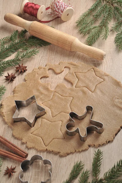 Noel kurabiyeleri pişiriyorum. Hamur ve kurabiye kesiciler. Ladin dalları, tarçın, anason kompozisyonu tamamlar. Dikey çerçeve yönlendirmesi. Açık arka plan.