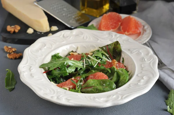 Pembe greyfurtlu salata. Bir parça Parmesan peyniri ve greyfurt dilimleri ile bir tabak ile tahta yakınında. Çerçevede ceviz, bir çatal ve bir peçete. Makro fotoğrafçılık.
