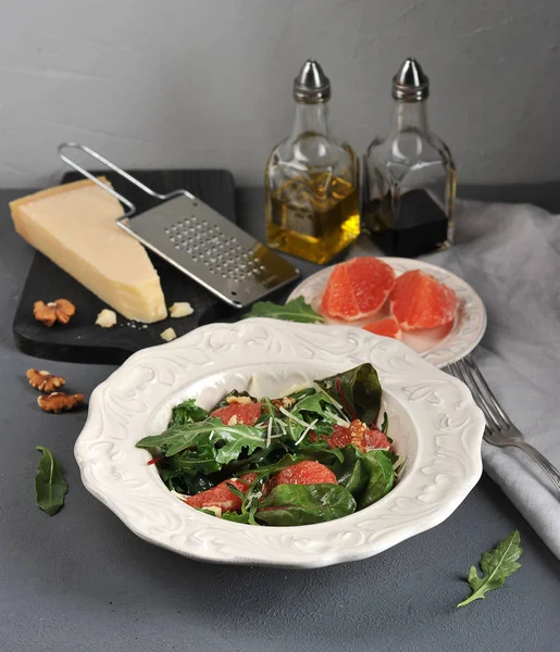 Pembe greyfurtlu salata. Bir parça Parmesan peyniriyle tahtanın yanında. Çerçevede ceviz, zeytinyağı ve balzamik sirke ile şişe. Yukarıdan görüntüleyin. Dikey çekim.