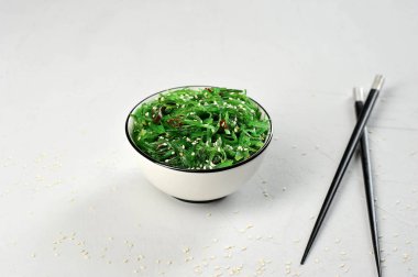 Beyaz bir kapta yosun salata chuka. Salata susam serpilir. Çerçevenin içinde, yemek çubukları. Açık arka plan. Close.