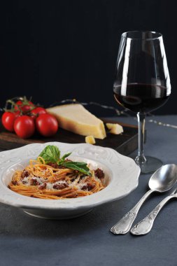 Bolonya soslu spagetti. Makarna fesleğen ile dekore edilmiş ve Parmesan peyniri serpilir. Kırmızı şaraplı bir bardağın yanında. Close. Çerçevenin dikey yönü.