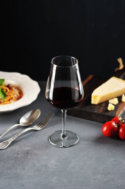 Bolonya soslu spagetti. Makarna fesleğen ile dekore edilmiş ve Parmesan peyniri serpilir. Kırmızı şaraplı bir bardağın yanında. Close. Çerçevenin dikey yönü.