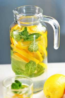 Limonve naneli portakaldan ev yapımı limonata. Çerçevede, limonatalı bir sürahi, bir bardak ve bir limon. Çerçevenin dikey yönü. Close. Makro fotoğrafçılık.