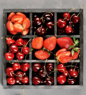 Çilek ve tatlı kiraz olgun çilek ile bir kutu. Kutu bölümlere ayrılmıştır. Yukarıdan görüntüleyin. Close. Gri arka plan. 