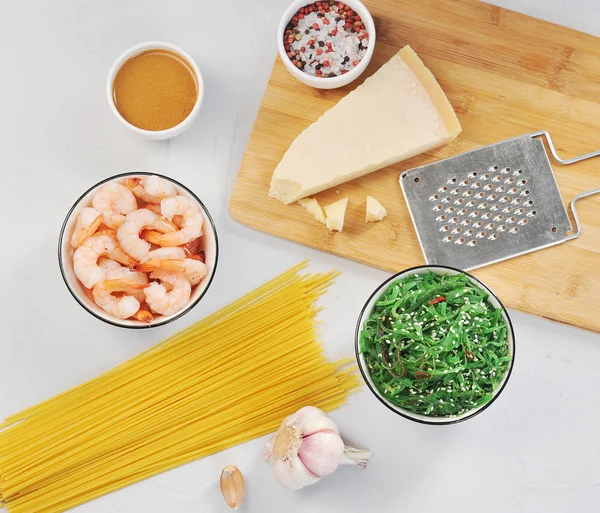 A set for cooking pasta with shrimps and seaweed. Spaghetti, chicken salad, shrimp, spices, garlic, nut sauce, parmesan cheese and grater for cheese. Light background. Close-up. View from above.