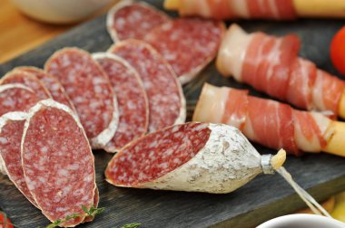 Tahta bir tahtada ekmek çubuklarının üzerine pastırma. Salam dilimleri ve bir kiraz domates dalı yanında. Close. Makro fotoğrafçılık.