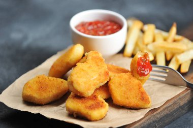 Tahta tahtada tavuk külçeleri ve patates kızartması. Bir sonraki bardak ketçap. Külçelerden biri çatala sabitlenmiş. Close. Gri arka plan. Makro fotoğrafçılık.
