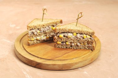 Ahşap bir tepsi üzerinde üçgen şeklinde iki sandviç. Sandviçler şişlerle sabitlenir. Sandviçin dolgusu mısır ve ton balığından oluşur. Close. Açık arka plan.