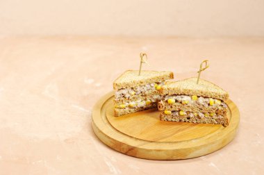 Ahşap bir tepsi üzerinde üçgen şeklinde iki sandviç. Sandviçler şişlerle sabitlenir. Sandviçin dolgusu mısır ve ton balığından oluşur. Close. Açık arka plan. Metin için boş alan.