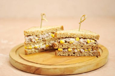 Ahşap bir tepsi üzerinde üçgen şeklinde iki sandviç. Sandviçler şişlerle sabitlenir. Sandviçin dolgusu mısır ve ton balığından oluşur. Close. Açık arka plan. 