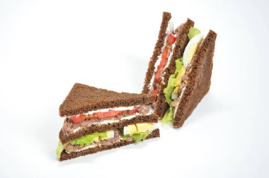 Sandwich with tuna, lettuce, egg and tomato slices. Slices of dark bread are smeared with soft ricotta cheese. The sandwich is cut diagonally into two parts. White background. Close-up.