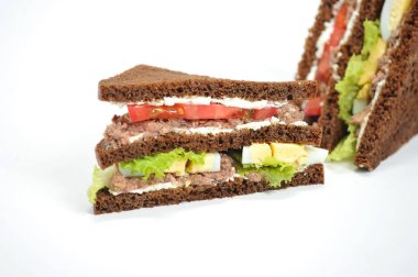 Sandwich with tuna, lettuce, egg and tomato slices. Slices of dark bread are smeared with soft ricotta cheese. The sandwich is cut diagonally into two parts. White background. Close-up.
