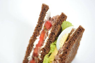Sandwich with tuna, lettuce, egg and tomato slices. Slices of dark bread are smeared with soft ricotta cheese. White background. Close-up.