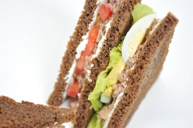Sandwich with tuna, lettuce, egg and tomato slices. Slices of dark bread are smeared with soft ricotta cheese. White background. Close-up.