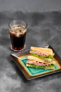 Beyaz ekmekten jambon ve peynirli sandviç. Dilimlenmiş ekmek kızartılır. Gazlı içecekle bardağın yanında. Gri arka plan. Close. Çerçevenin dikey yönü.