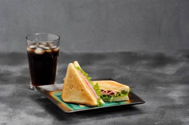 Jambon ve peynir ile üçgen şeklinde Sandviçler. Beyaz ekmek dilimleri kavrulur. Gazlı içecekle bardağın yanında. Gri arka plan. Close.