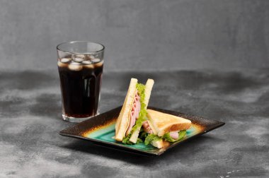 Jambon ve peynir ile üçgen şeklinde Sandviçler. Beyaz ekmek dilimleri kavrulur. Gazlı içecekle bardağın yanında. Gri arka plan. Close.