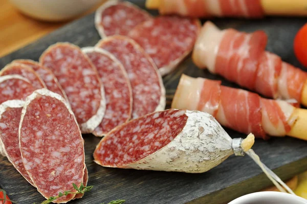 Tahta bir tahtada ekmek çubuklarının üzerine pastırma. Salam dilimleri ve bir kiraz domates dalı yanında. Close. Makro fotoğrafçılık.