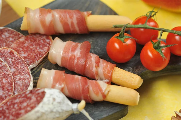 Tahta bir tahtada ekmek çubuklarının üzerine pastırma. Salam dilimleri ve bir kiraz domates dalı yanında. Close. Makro fotoğrafçılık.