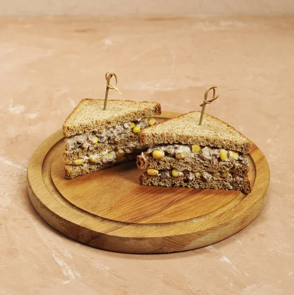 Ahşap bir tepsi üzerinde üçgen şeklinde iki sandviç. Sandviçler şişlerle sabitlenir. Sandviçin dolgusu mısır ve ton balığından oluşur. Close. Açık arka plan.