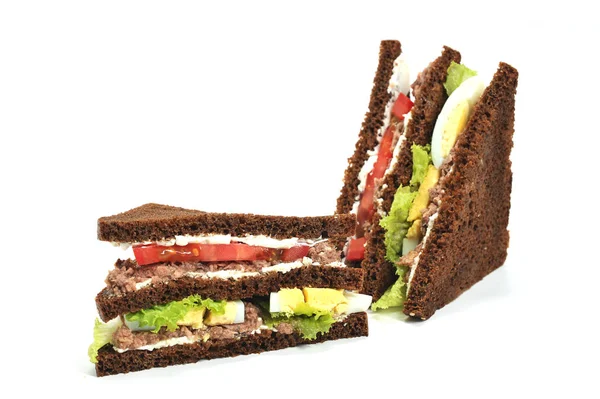 Sandwich with tuna, lettuce, egg and tomato slices. Slices of dark bread are smeared with soft ricotta cheese. The sandwich is cut diagonally into two parts. White background. Close-up.