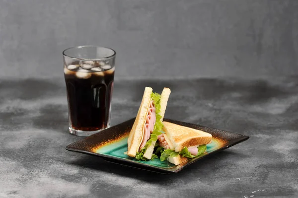 Jambon ve peynir ile üçgen şeklinde Sandviçler. Beyaz ekmek dilimleri kavrulur. Gazlı içecekle bardağın yanında. Gri arka plan. Close.