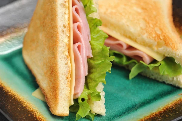 Bir tabakta üçgen şeklinde sandviçler. Sandviçin dolgusu jambon, peynir ve yapraklardan oluşur. Beyaz ekmek parçaları kızartılmış. Close. Makro fotoğrafçılık.