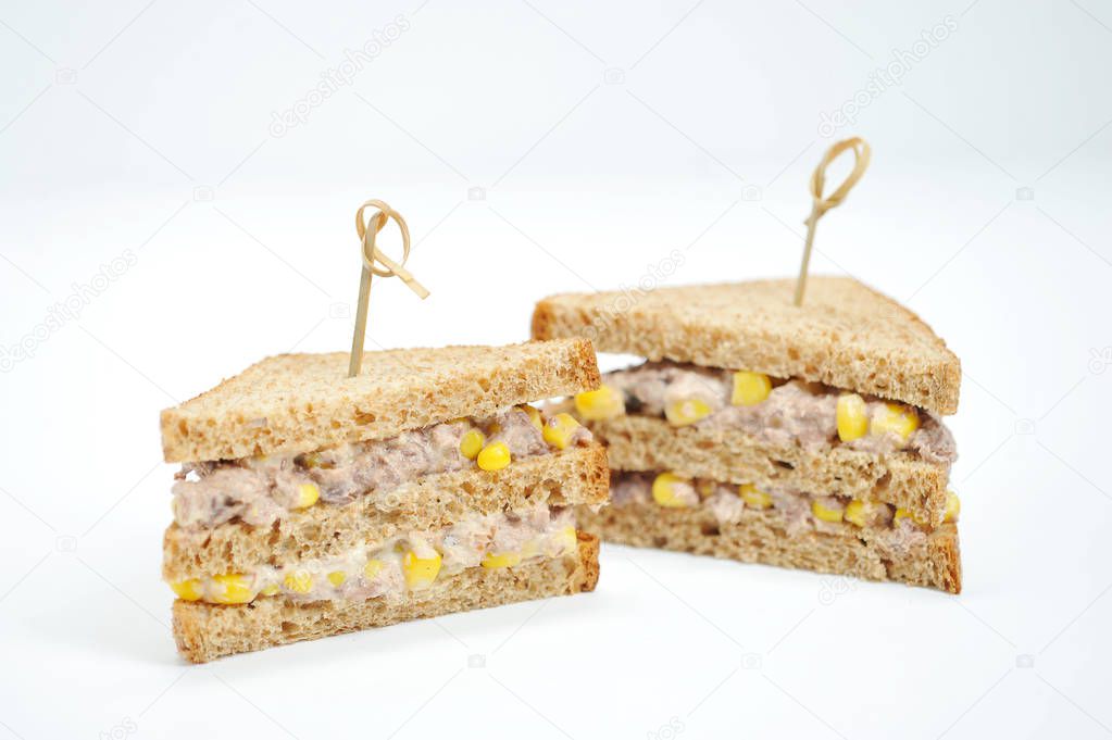 Two sandwiches of a triangular shape on a white background. The filling of the sandwich consists of corn and tuna. Close-up.