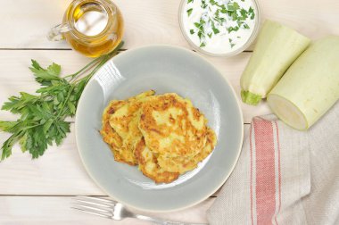 Tabaktaki kabaktan küçük krepler. Yemeğin yanında bir peçete, bir çatal, bir demet maydanoz, zeytinyağı ile bir sürahi ve ekşi krema soslu bir fincan vardır. Açık arka plan. Yukarıdan görüntüle.