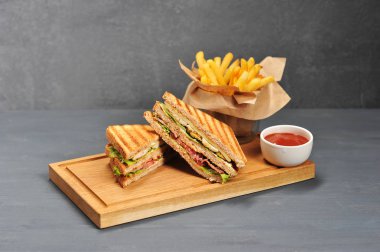 Pastırma, tavuk göğsü, peynir ve taze sebze dolum ile iştah açıcı ve besleyici sandviç. Tamamlayıcı sandviç gevrek patates kızartması ve ketçap. Gri arka plan. Close.