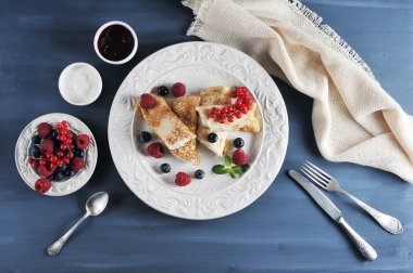 Krep, süzme peynirle doldurulmuş. Yemek ahududu, yaban mersini ve kırmızı kuş üzümü meyveleri ile dekore edilmiştir. Çerçeve reçel, ekşi krema, çilek ile bir tabak. Close. Yukarıdan görüntüle.