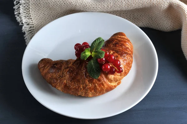 Puf böreği yapılmış hava kruvasan. Kruvasan kırmızı frenk üzümü meyveleri ile bir dal ile dekore edilmiştir. Çerçeve bez peçete içinde. Koyu ahşap arka plan. Close.