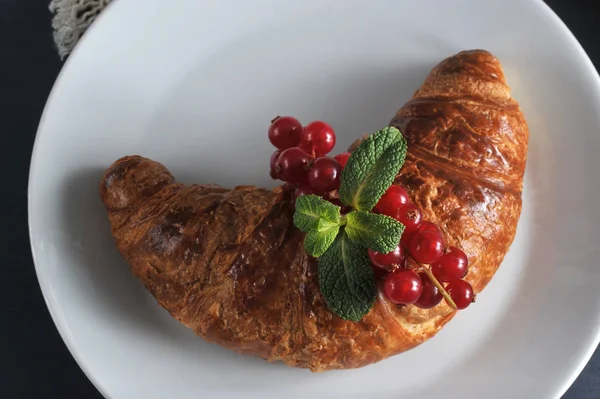 Puf böreği yapılmış hava kruvasan. Kruvasan kırmızı frenk üzümü meyveleri ile bir dal ile dekore edilmiştir. Çerçeve bez peçete içinde. Koyu ahşap arka plan. Close.