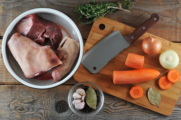 Et jölesi yapmak için bir set. Bir kasede, domuz eklemi ve sığır gümüş tarafı. Havuç, soğan, defne yaprağı, sarımsak, bir demet kekik, et kesmek için bir bıçak. Ahşap arka plan. Yukarıdan görüntüle.