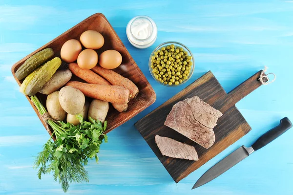 Salata olivier hazırlanması için ayarlayın. Tabakta haşlanmış yumurta, patates, havuç, salatalık turşusu, yeşillik. Mayonez konservesinin yanında, bir tabak yeşil bezelye ve haşlanmış sığır eti. Yukarıdan görüntüle.