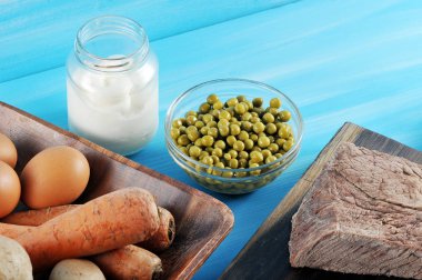 Salata olivier hazırlanması için ayarlayın. Çerçeveiçinde haşlanmış yumurta, patates, havuç, salatalık turşusu ile bir tabak vardır. Mayonez konservesinin yanında, bir tabak bezelye ve haşlanmış sığır eti. Mavi arka plan