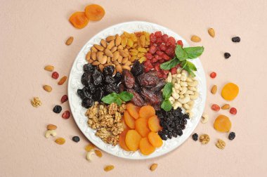 Büyük beyaz bir tabak üzerinde fındık ve kurutulmuş meyve. Kuru üzüm, kuru kayısı, kuru erik, hurma, kiraz, kaju fıstığı, badem, ceviz bir tabak üzerinde. Açık arka plan. Close. Yukarıdan görüntüle.